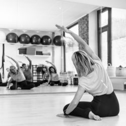 Posture de pilates: josiane buchart face au miroir de la salle du studio pilates et yoga satigny en position du stretching sur le coté avec un groupe d'élèves hommes et femmes